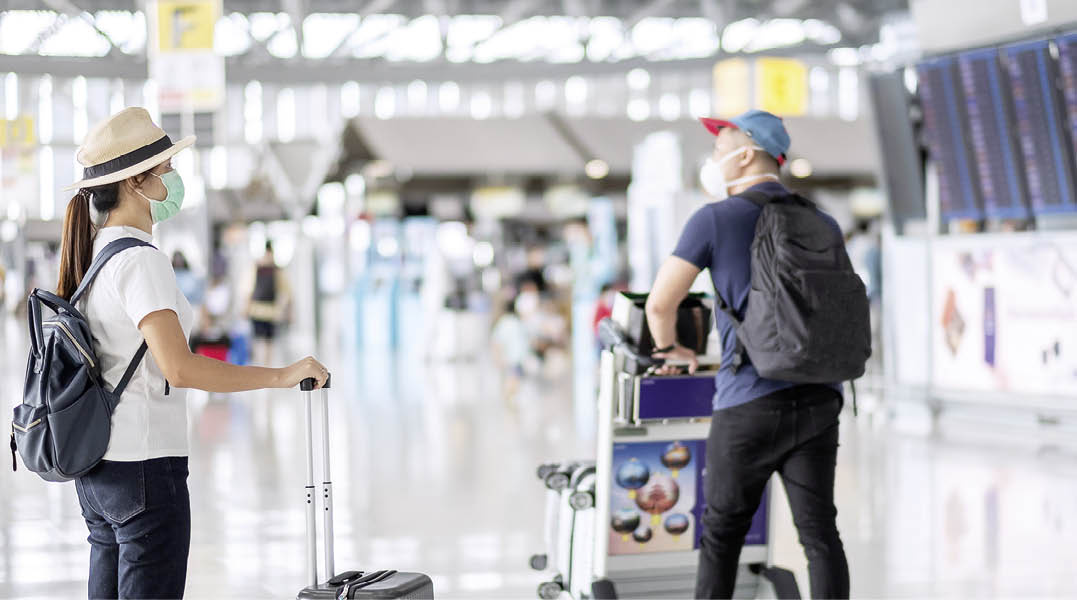 Young female wearing face mask with luggage checking flight time in airport, protection Coronavirus disease (Covid-19) infection, Asian woman traveler with hat  New Normal and travel bubble concept